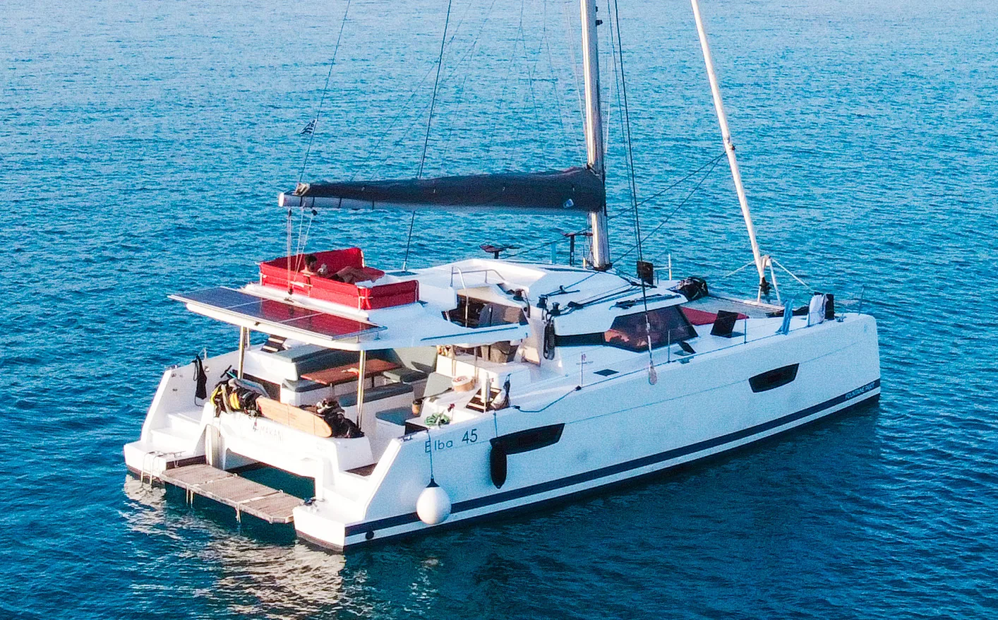 Aerial view of the Makani catamaran anchored alone on deep blue open water.
