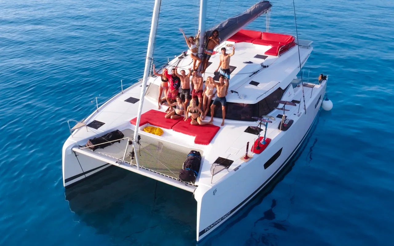 Aerial view of the Makani luxury catamaran with the whole group relaxing across its sundecks on calm blue water.